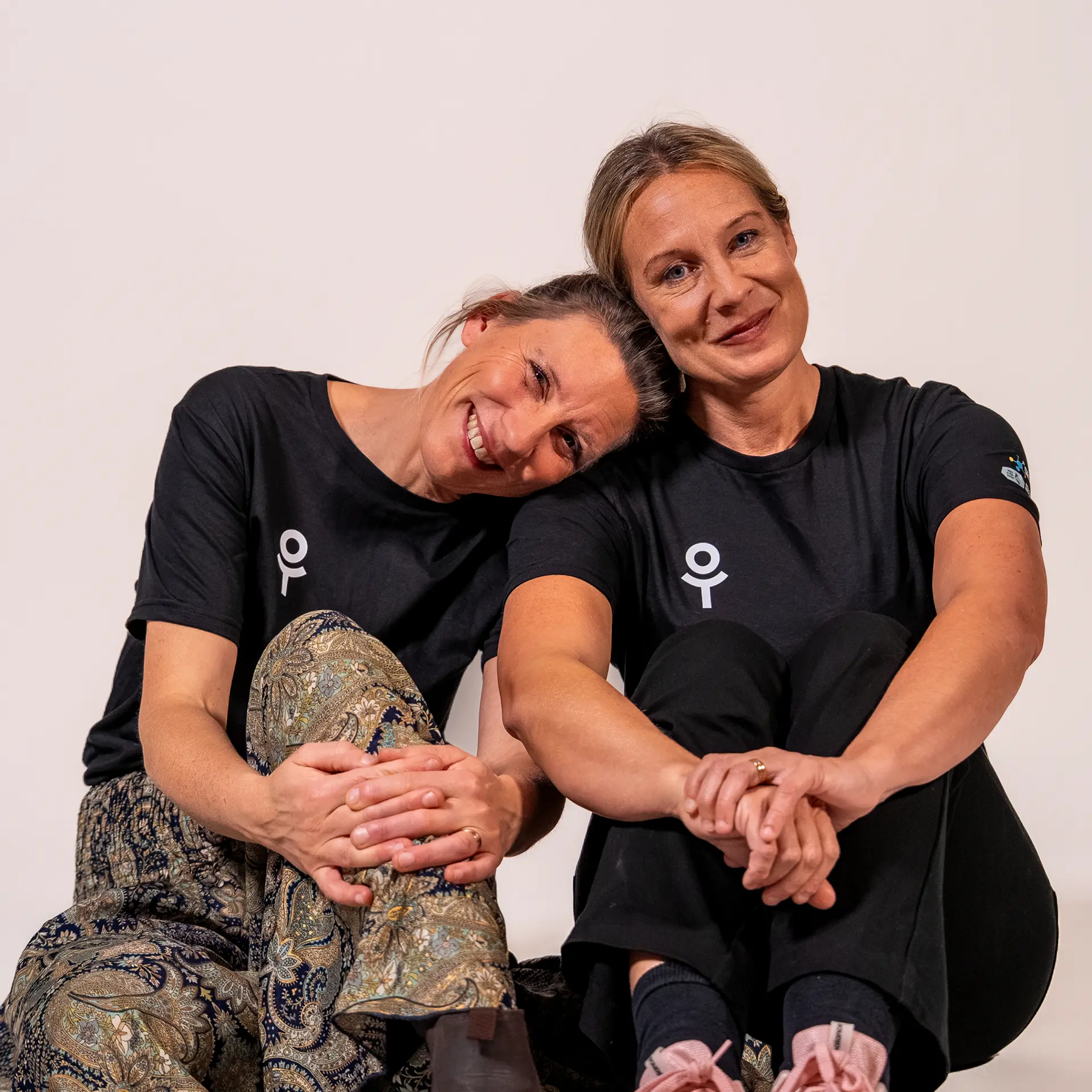 Två kvinnor i On Track-tröjor sitter tätt intill varandra och ler mot kameran.