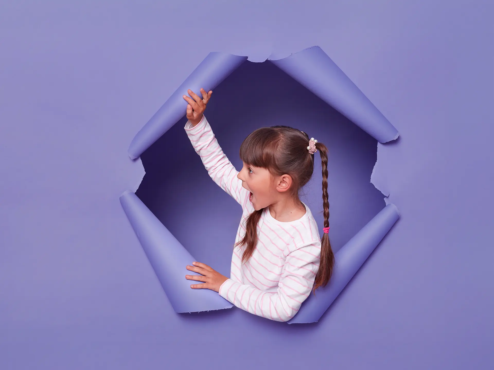 En glad flicka med flätad hästsvans sticker upp ur ett hål ur väggen.