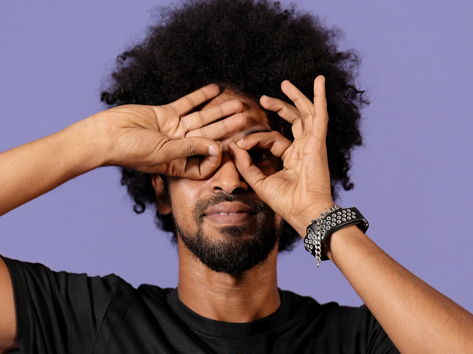 En man i On Track-tröja håller händerna framför ögonen som kikare och poserar framför en lila bakgrund.